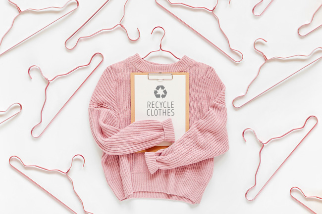 image of empty jumper holding a sign saying recycle clothes with coat hangars in the background